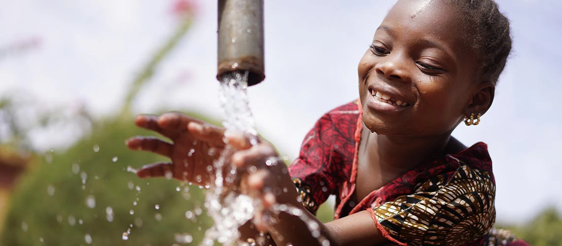 A little girl playing with water coming out of a pipe 