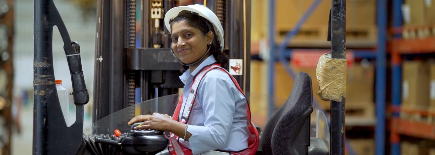 A woman operates a high-reach stacker with ease in a Pune warehouse. 