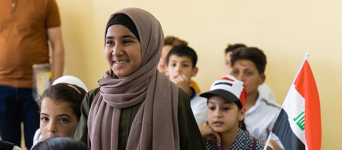 A student stands amongst her classmates in a classroom in Iraq.