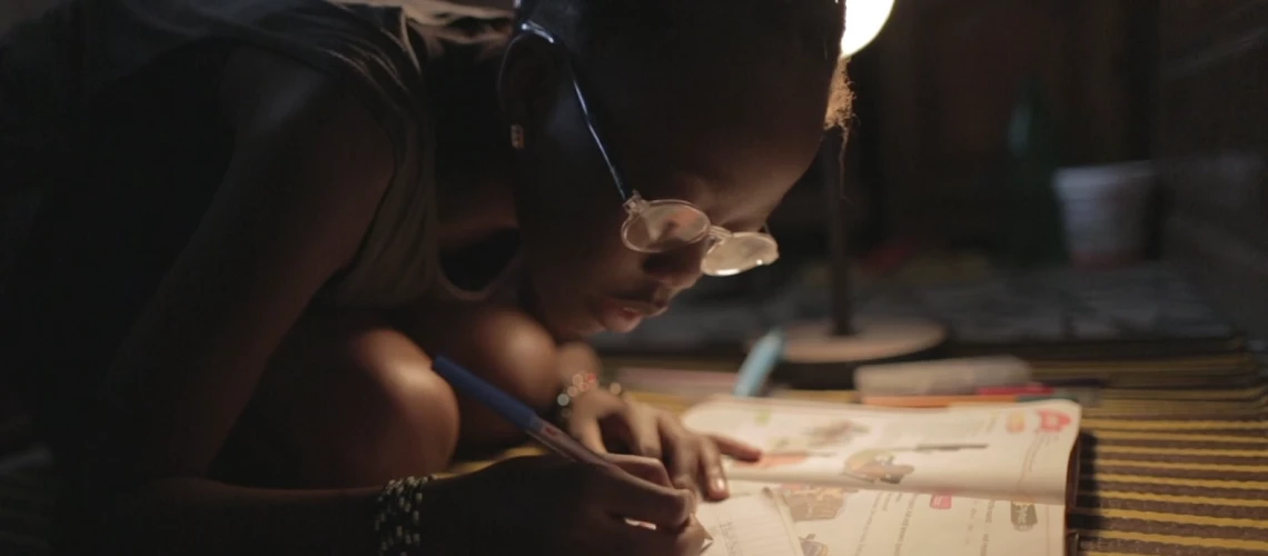 A young Senegalese girl doing homework under the light of a lamp.