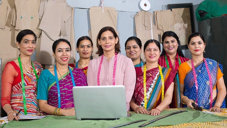 Group of Indian woman using laptop by sewing machine at textile factory