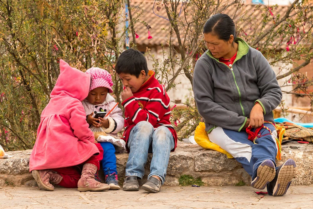 Woman sitting with her children playing with a phone in rural Peru. Credit: nmessana/iStock