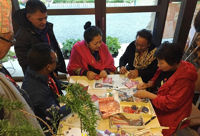 Community members from Nepal learn how to make paper jewelry crafts from Ibasho-Japan elders. 