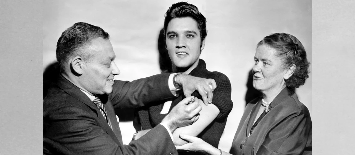 Elvis Presley receiving a polio vaccination from Dr. Leona Baumgartner and Dr. Harold Fuerst at CBS studio 50 in New York City.