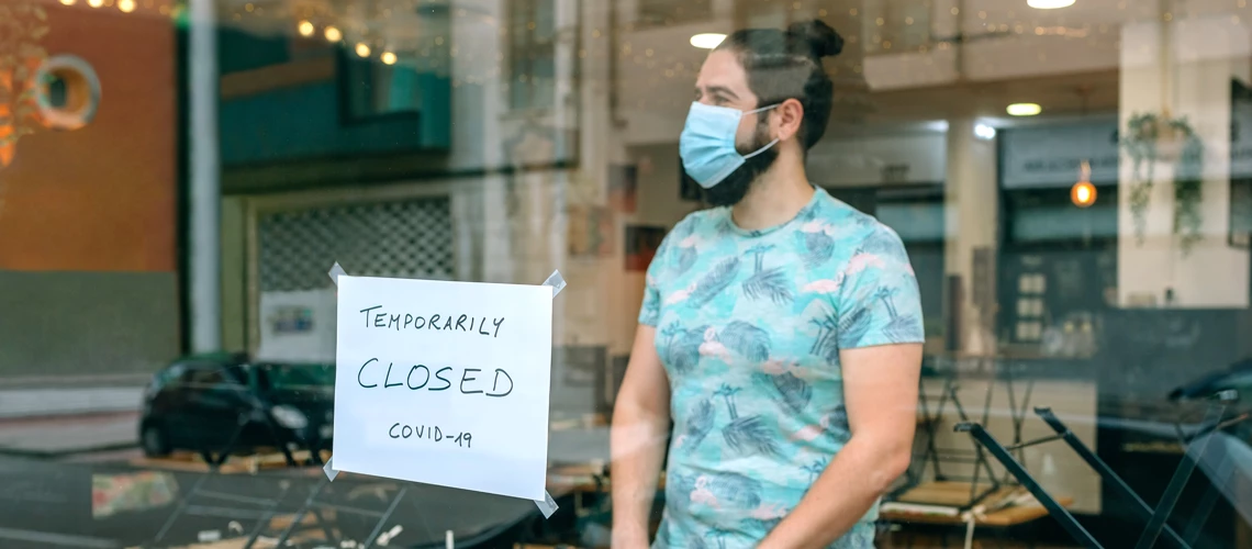 Thoughtful man with a mask behind the glass of his restaurant closed by COVID-19