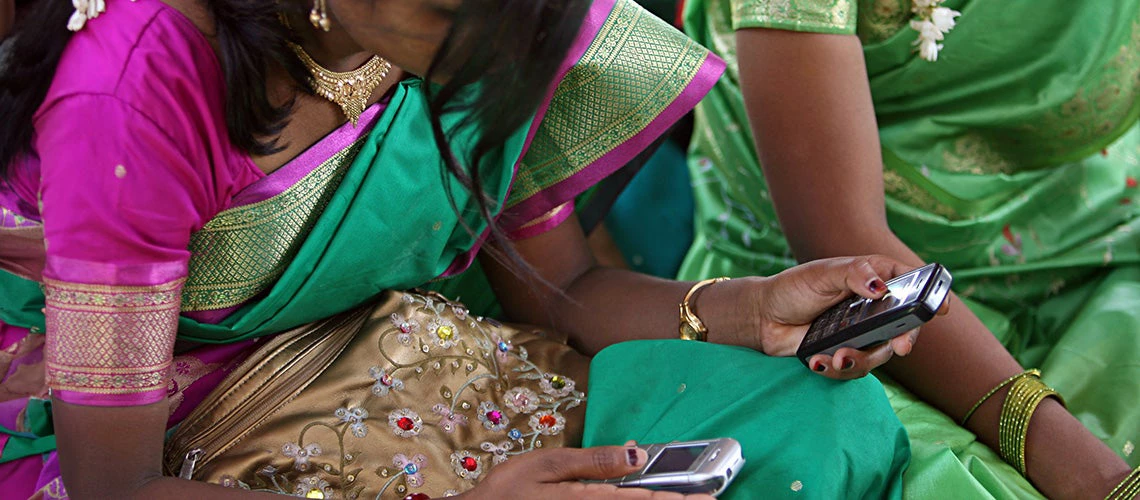 Young women look at their cellphone during a community meeting. | © Simone D. McCourtie / World Bank