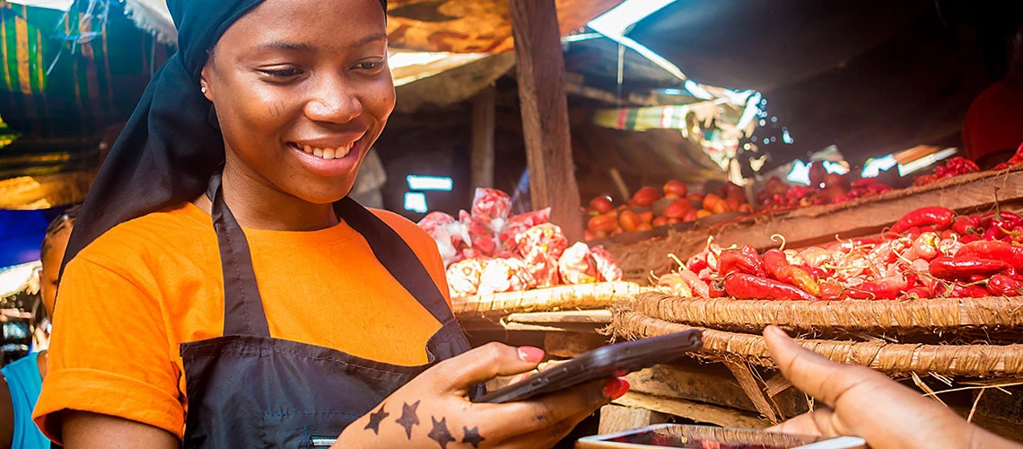 Young woman selling tomatoes in a local african market receiving payment via mobile phone transfer | © shutterstock.com