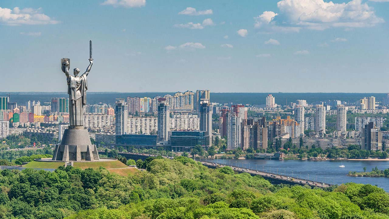 Motherland monument among green trees on embankment in Kiev.