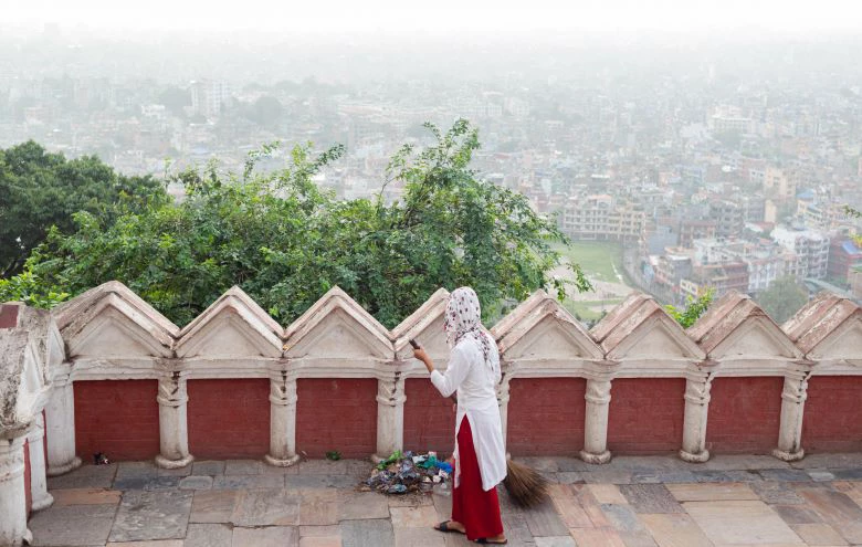 A woman holds a broom and sweeps garbage on a premises overlooking the Kathmandu Valley