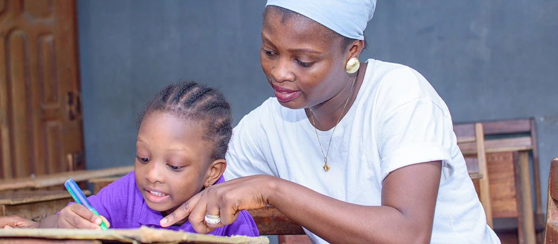 A mother/teacher helping a child in a classroom. | © shutterstock.com