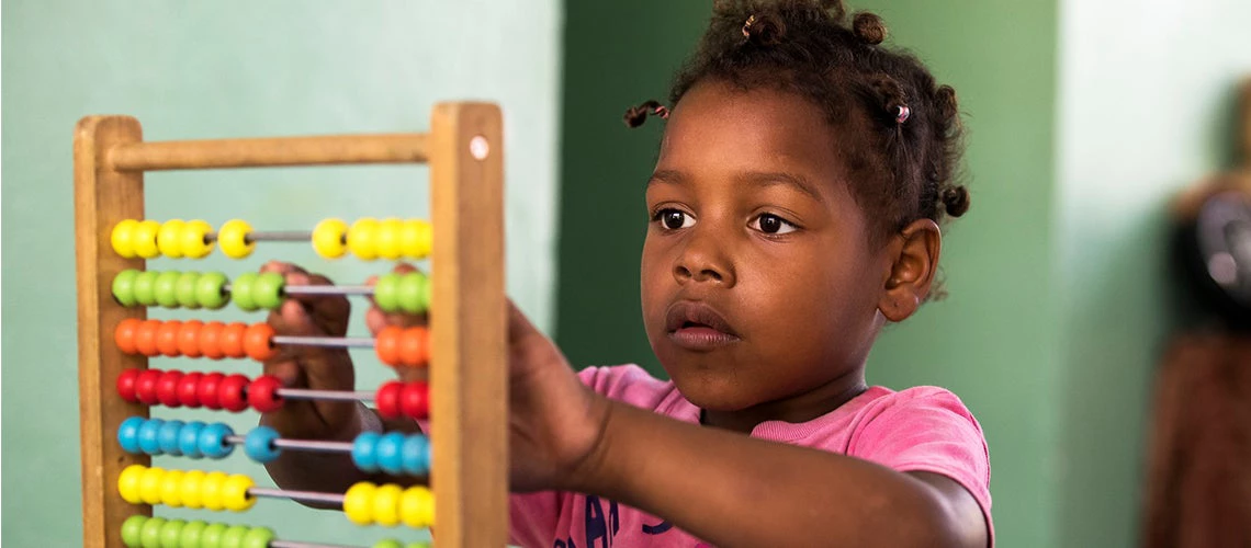 Niña aprendiendo matemáticas con un ábaco en una escuela de la República Dominicana