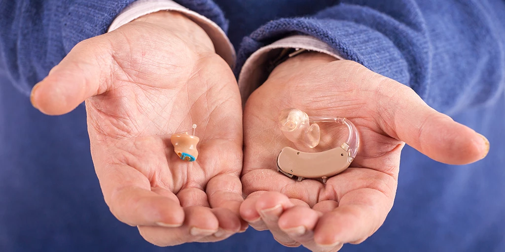 A person holds two hearing aids of different sizes.