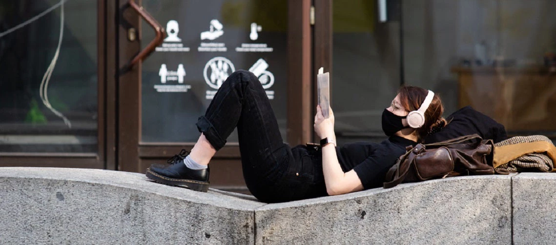 A young girl reading a book while lying on concrete on the street