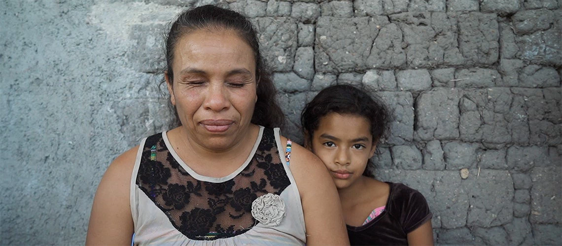 A blind woman poses in front of the camera with a girl