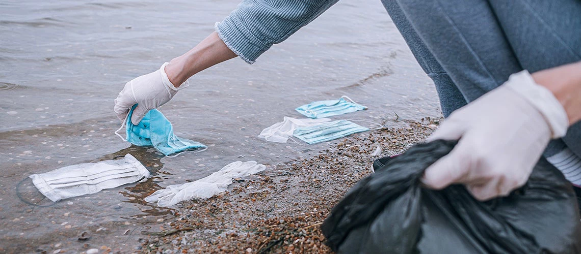 Female volunteer removes debris from used medical masks and gloves on the beach and in the water.