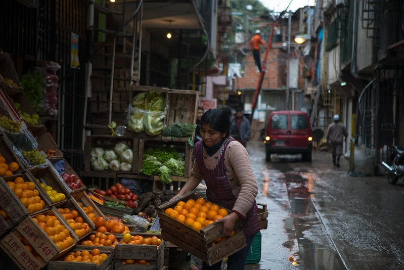 A woman carrying a basket of fruit in a greengrocer's shop