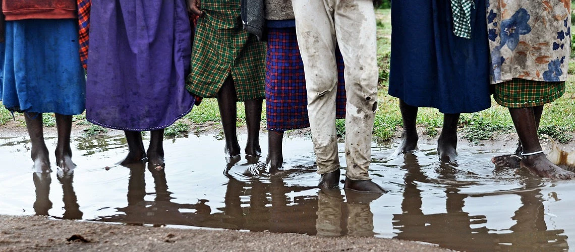 Children line up with their toes in a shallow puddle in Kenya.