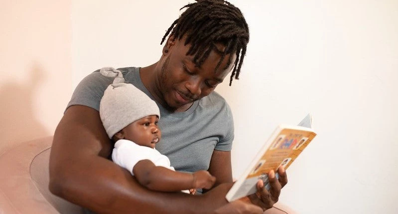 A photo of a man reading to an infant.