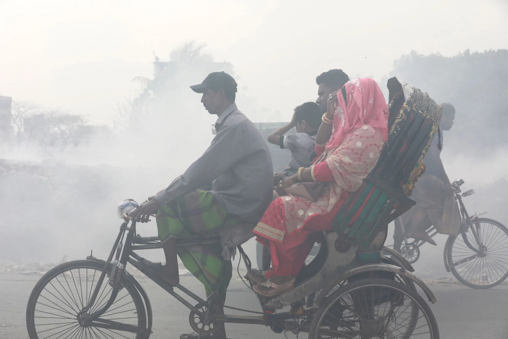 Picture of people riding through smoke from burning waste in Dhaka, Bangladesh.
