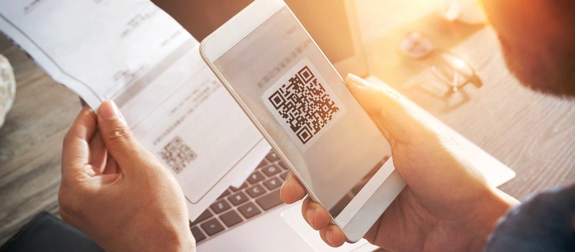 A man holding up a mobile phone to scan a QR code on an invoice.