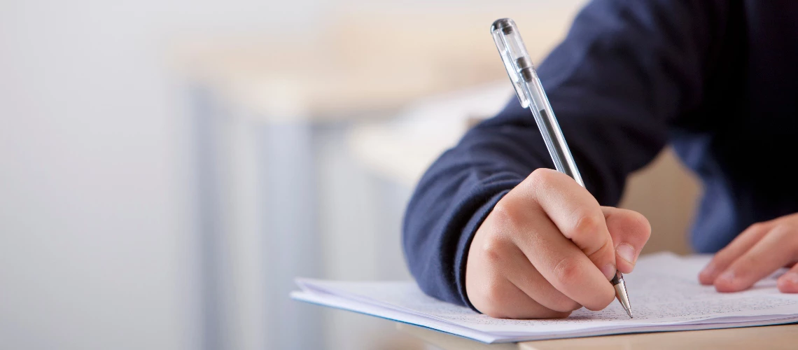 A close up shot of a student's hand writing exam at his desk