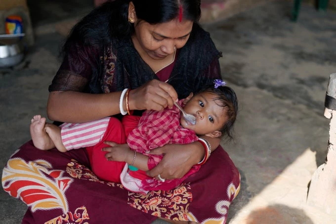 Indian Bengali tribal mother is feeding her baby on her lap in a rural background. Indian rural lifestyle