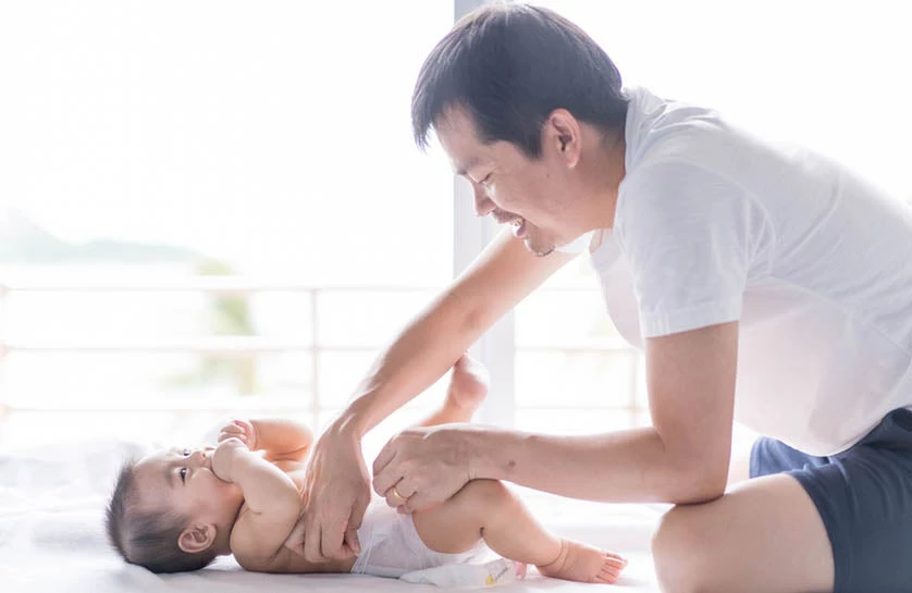 Photo of a young father is changing his baby's diaper.