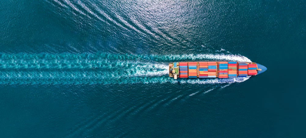 Aerial view of a maritime cargo ship in motion and producing a wake in the surrounding water.  Photo: GreenOak/Shutterstock