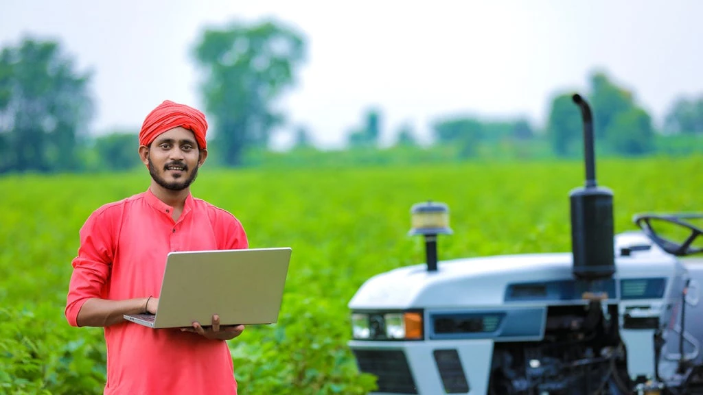 Technology and people concept : Young indian farmer using laptop at field 