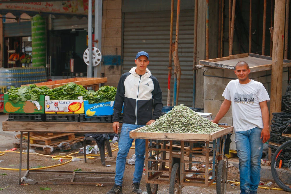 Two young Palestinian men vendors stand in front of their vegetable cart. (Shutterstock.com/ Abu Adel photo)