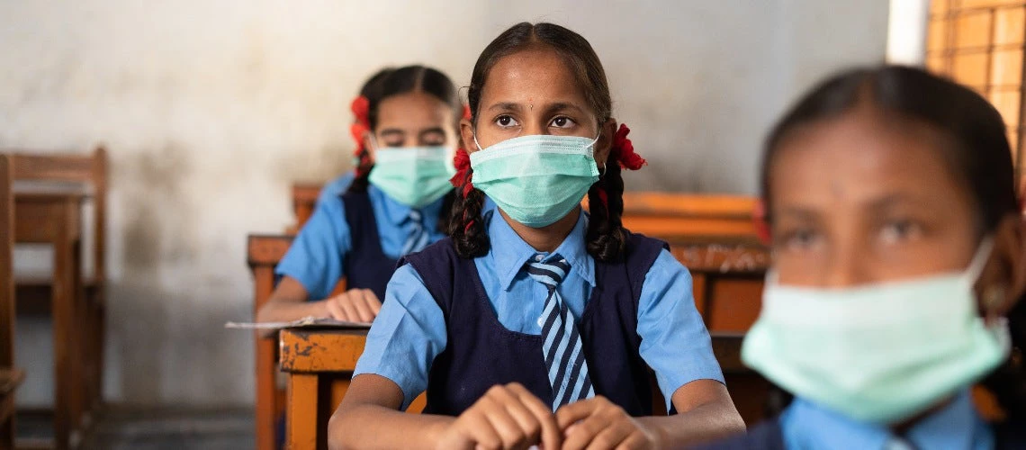 Girl kid with medical face mask listening class at school while maintaining social distance 