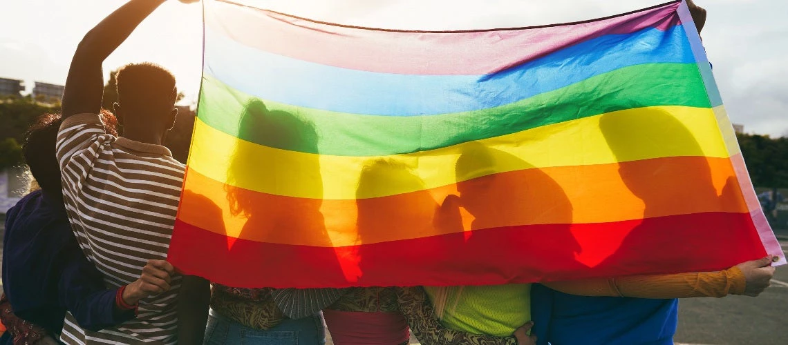 Young diverse people having fun holding lgbt rainbow flag outdoor