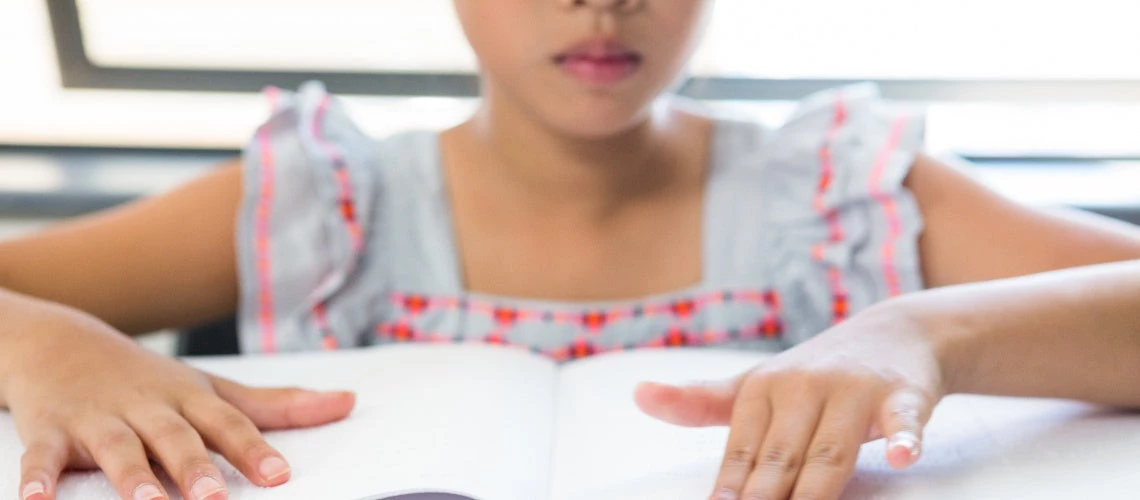 Midsection of blind girl reading braille book in classroom