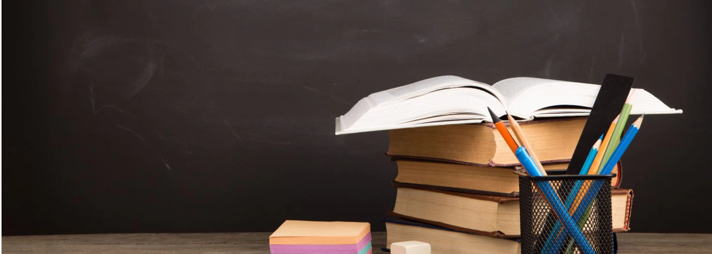 Pile of books on top of a desk and pens.