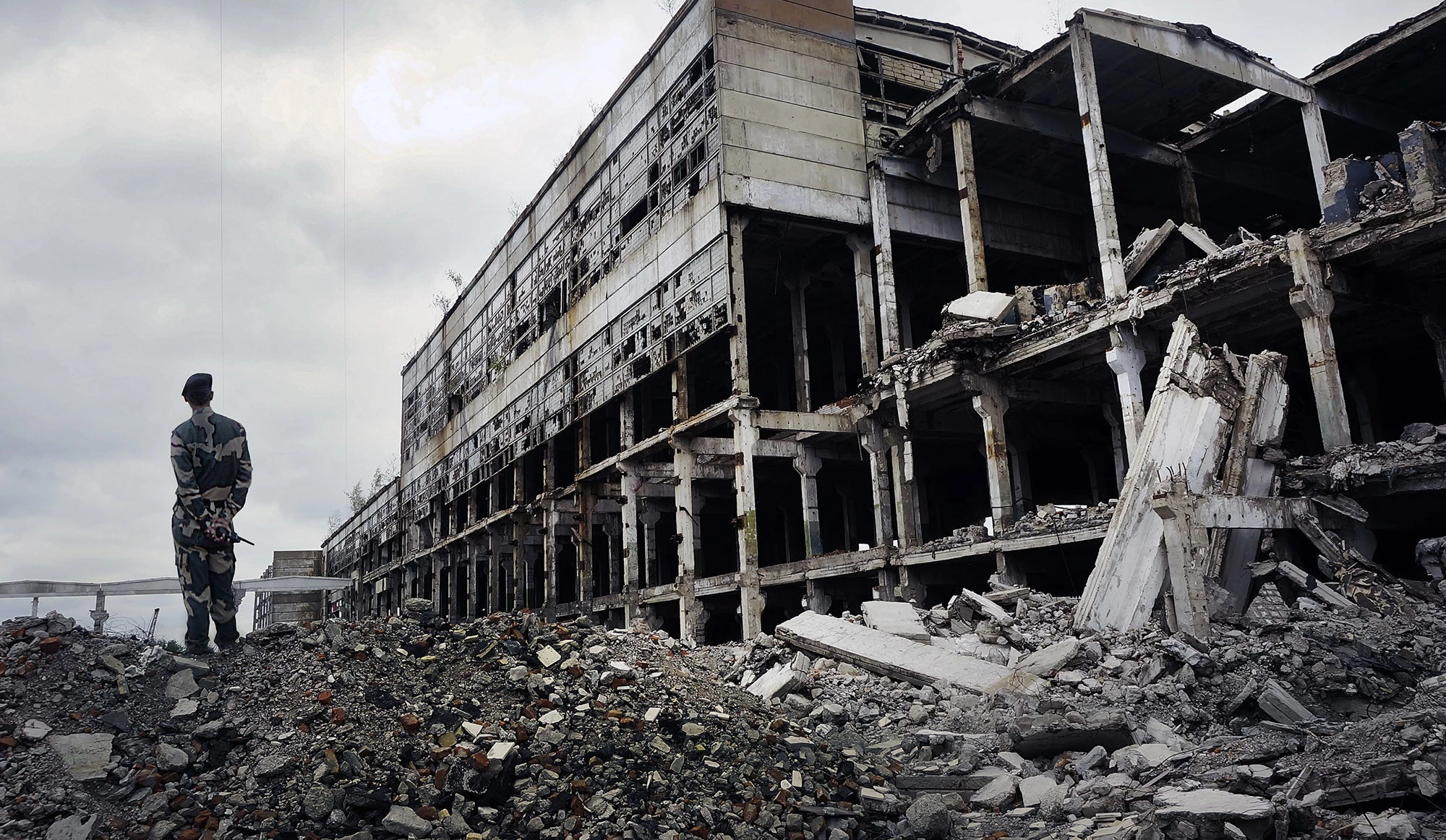 Soldier in military uniform stands on the ruins of the destroyed house. 