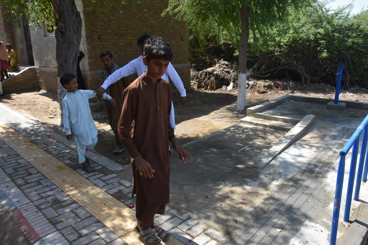 A visually impaired boy in Sindh uses cane and tactile paving to navigate through his village