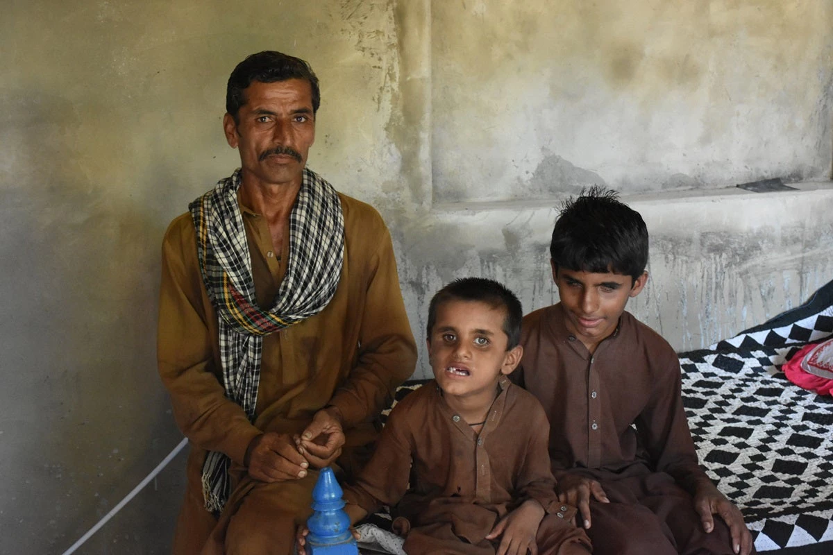 A father from Sindh sitting with his two sons who are visually impaired in their village home