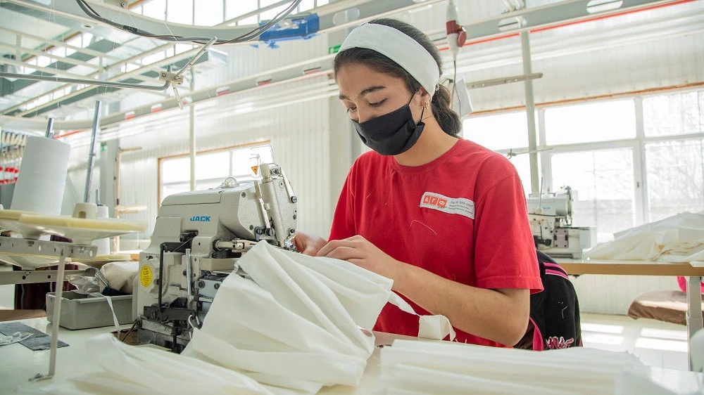 Women workers in a garment factory with medical masks on their faces sew protective masks during the COVID-19 virus pandemic. 