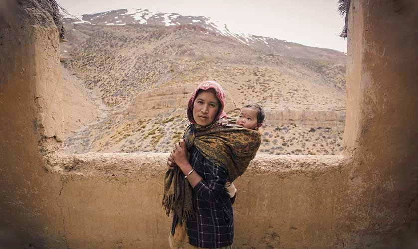 Photo of an Indian woman carrying her b aby on her back in Spiti Valley.