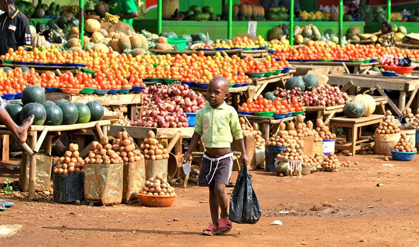 African young boy walking with a plastic bag through a fruit and vegetables market, Kampala, Uganda.