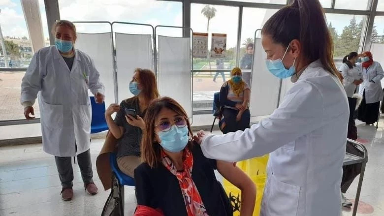 A female Tunisian doctor wearing a face covering is administering a vaccine to another Tunisian woman at a healthcare facility