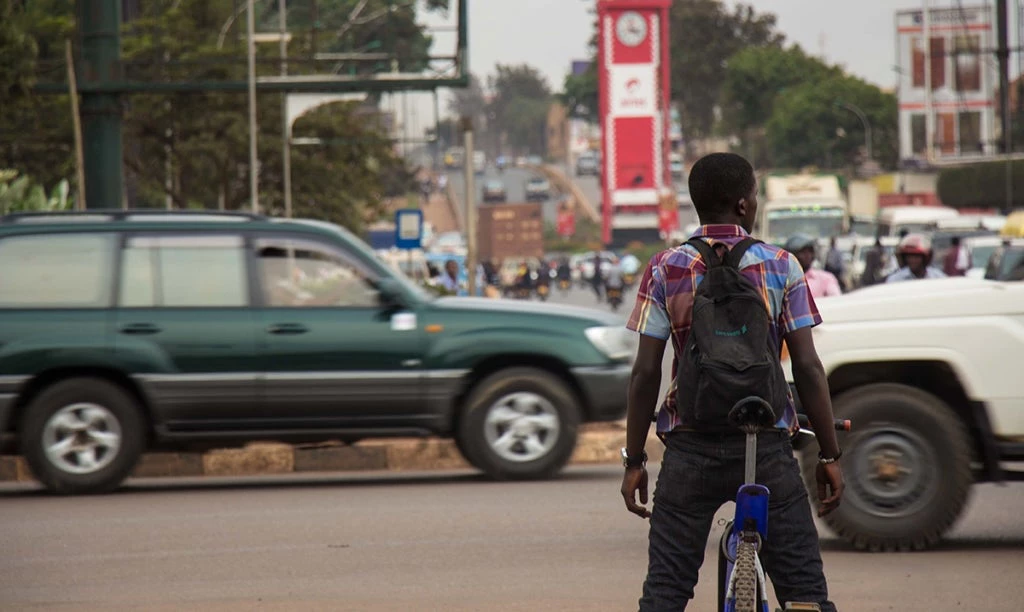 Young man on a bicycle waiting at a road junction in Kampala, Uganda. Photo: Sarah Farhat/World Bank