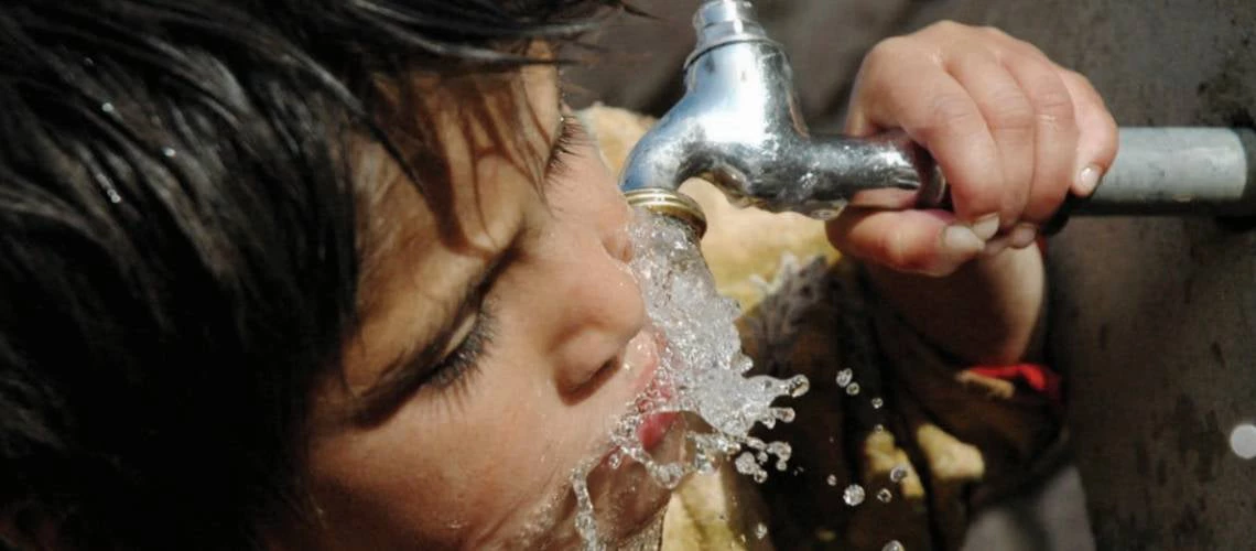 A child drinks water from a water pipe.