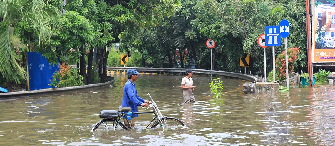 Man crossing a flooded street carrying his bike.