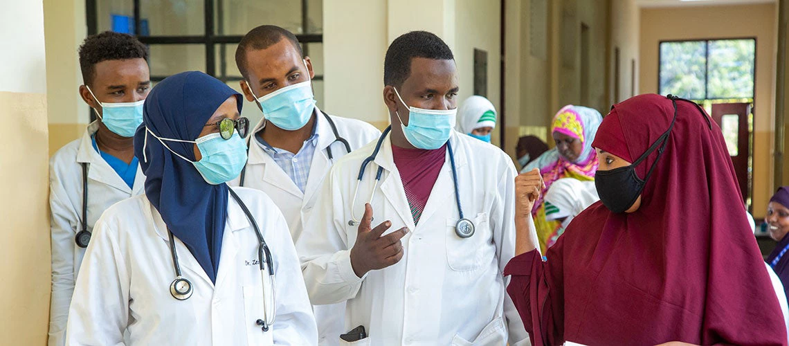 Doctors are walking along a hospital corridor discussing case and wearing face mask.