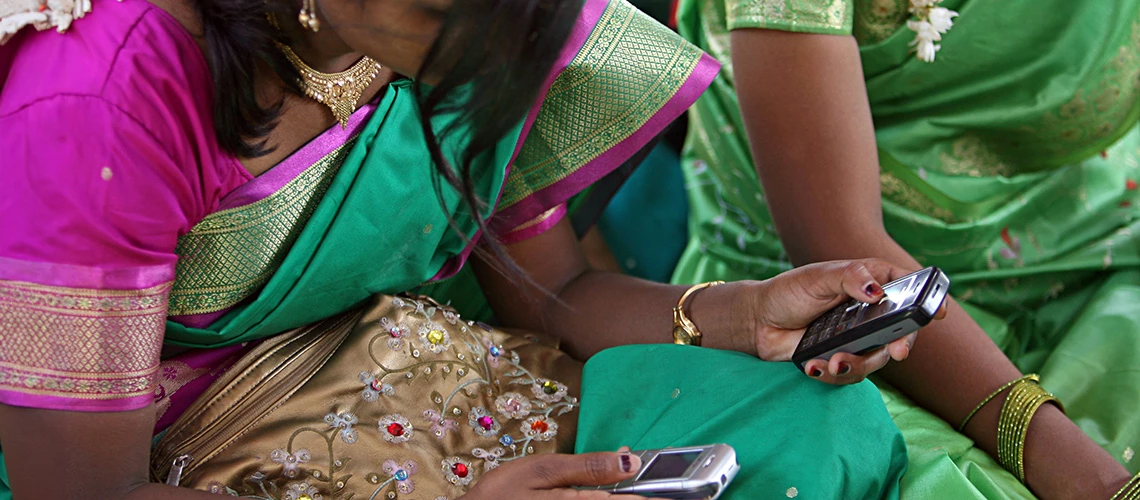 Young women look at their cellphone during a community meeting. | © Simone D. McCourtie / World Bank