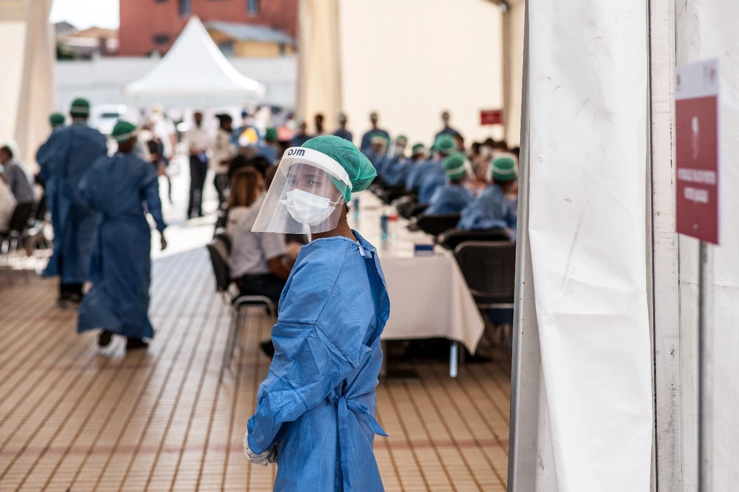 A healthcare worker wearing a protective face shield and a medical protective suit stands in the middle of a healthcare center