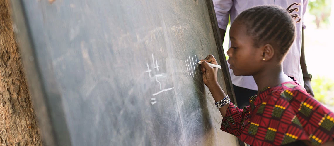 A girl is writing numbers on a blackboard during open air classes in a rural community in West Africa. | © shutterstock.com