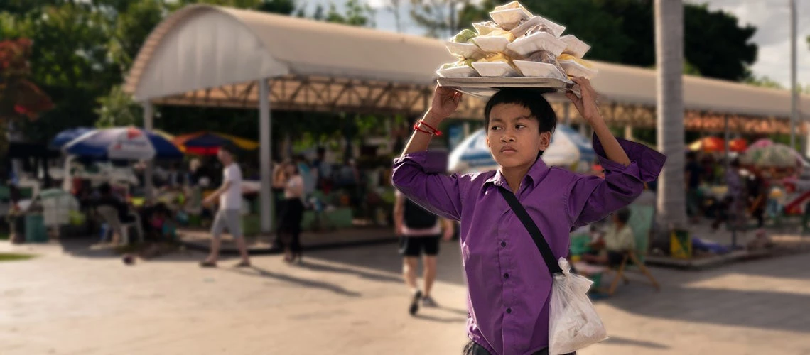 Young boy carries food containers on his head to be sold at a local market in Phnom Penh, Cambodia. | © shutterstock.com