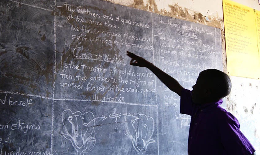 A young boy in school uniform pointing at the blackboard